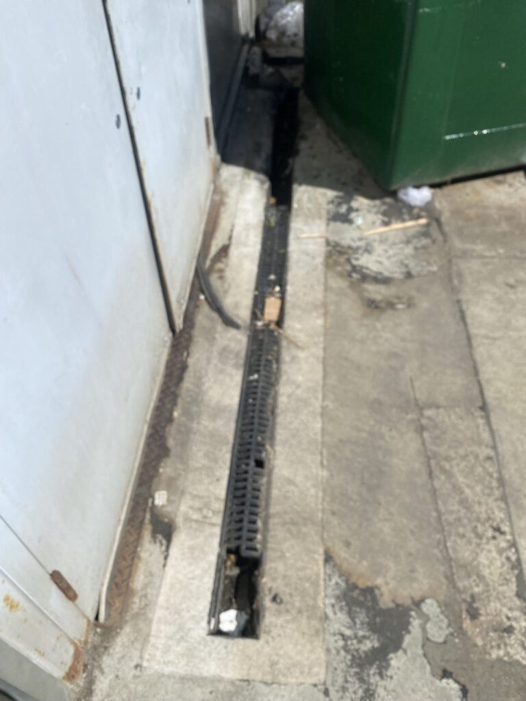 Clogged commercial channel drain in Burnaby showing debris and poor water flow