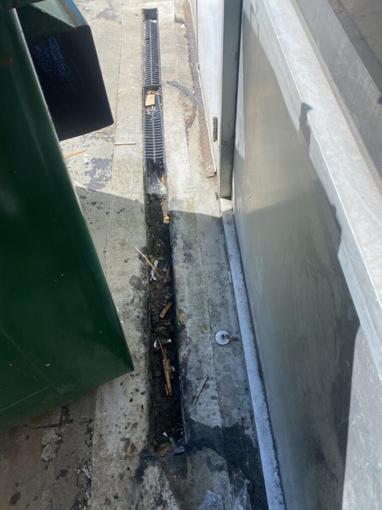 Clogged commercial channel drain in Burnaby showing debris and poor water flow