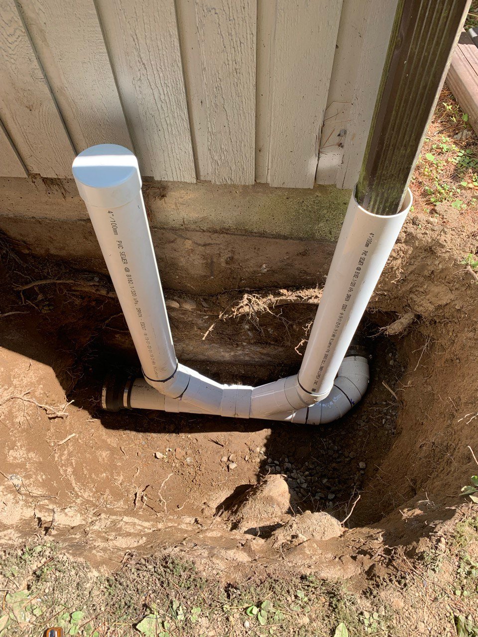 Underground downspout drain connection beside a house