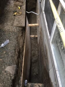 Trench excavation for French drain installation beside a home's foundation in Vancouver