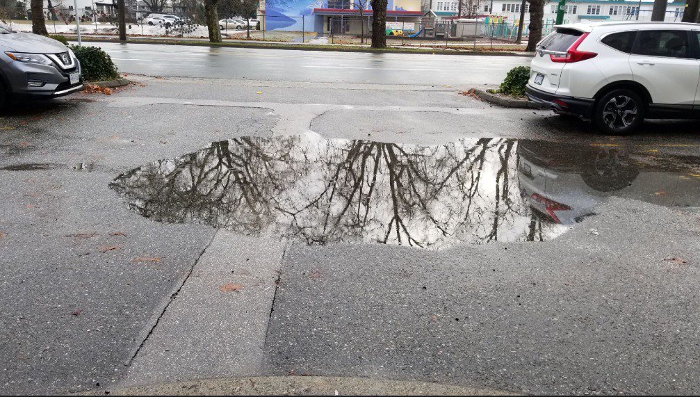 Water pooling around an exterior yard drain beside a home